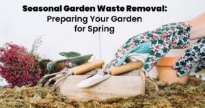 A gloved hand holds gardening tools above a wooden box surrounded by moss and plants, emphasizing spring garden preparation.